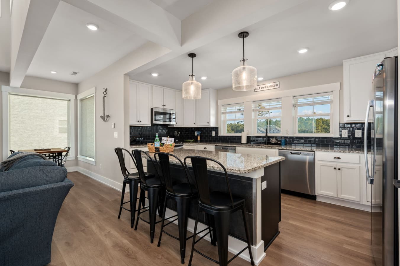 Open kitchen w/ granite island, pendant lighting & barstool seating beside the living space