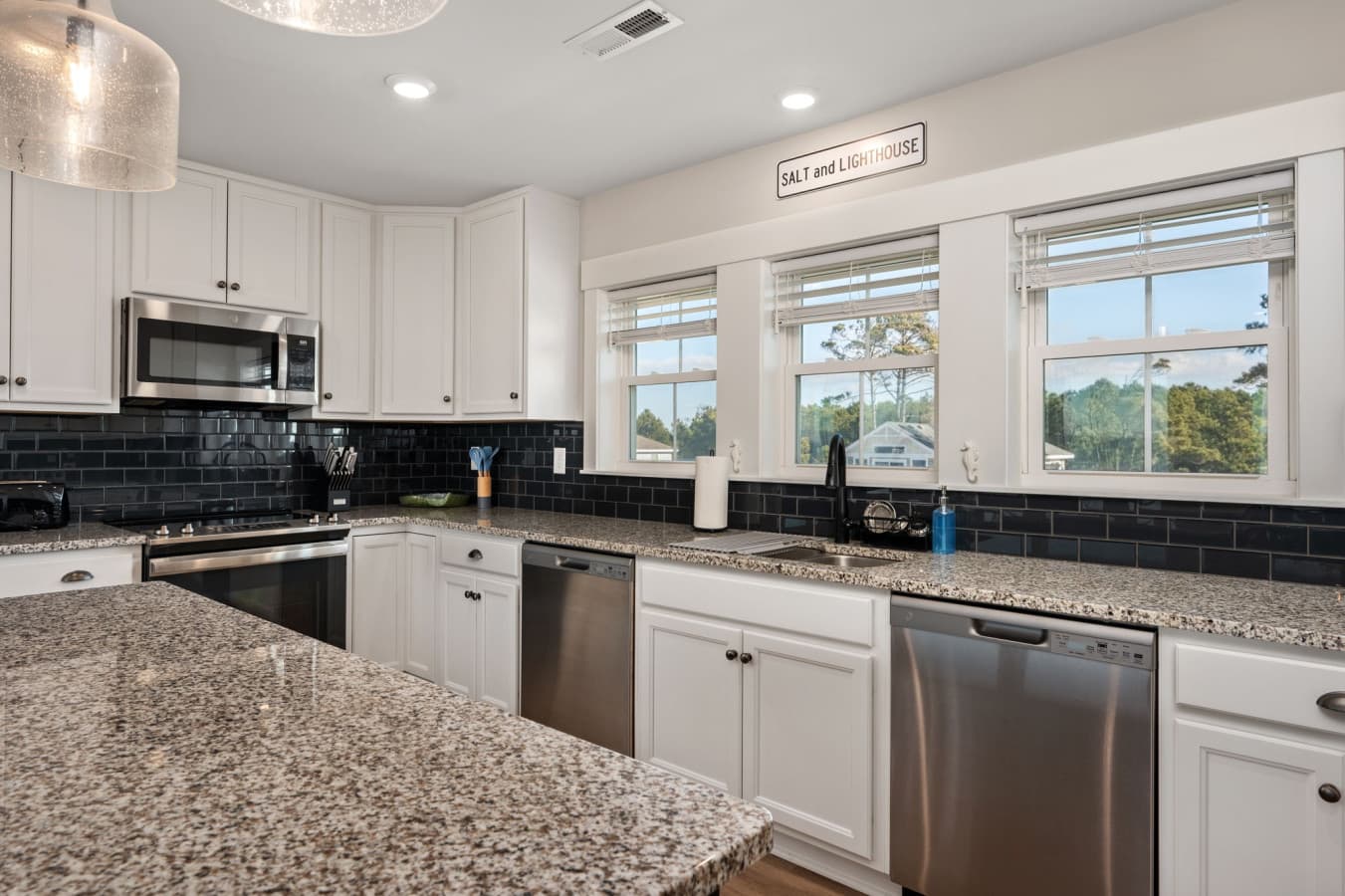 Kitchen w/ granite counters, dark subway backsplash & windows over the sink for daylight prep