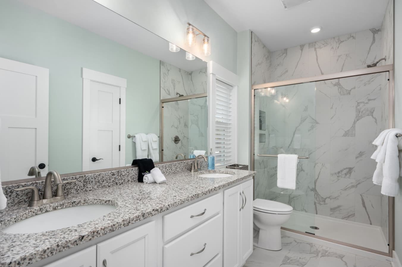 Bath w/ marble-tiled walk-in shower, granite vanity & glass enclosure for a spa feel