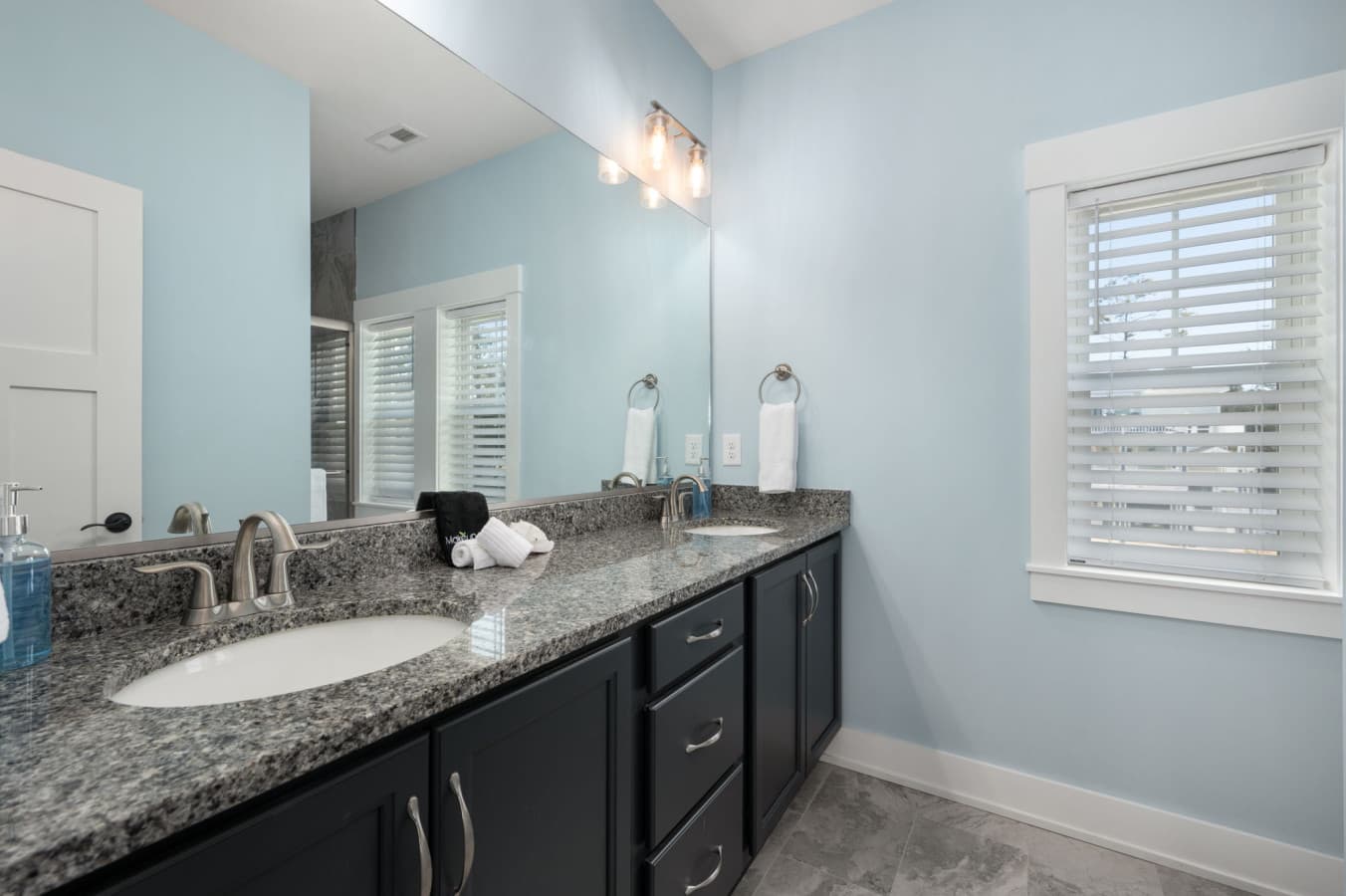 Bath w/ double granite vanity, dark cabinetry & a shuttered window for easy mornings