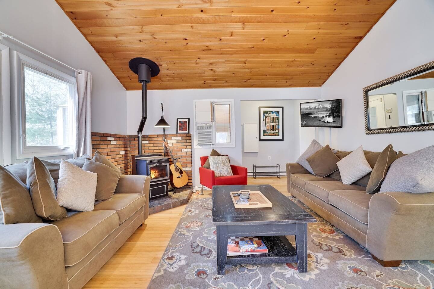 Cozy Cabin Living Room with Wood Stove 
Relax in this warm and inviting living room, featuring plush sofas, a crackling wood stove, and charming wood-paneled ceilings. Unwind with a book or strum a few tunes on the acoustic guitar provided. 