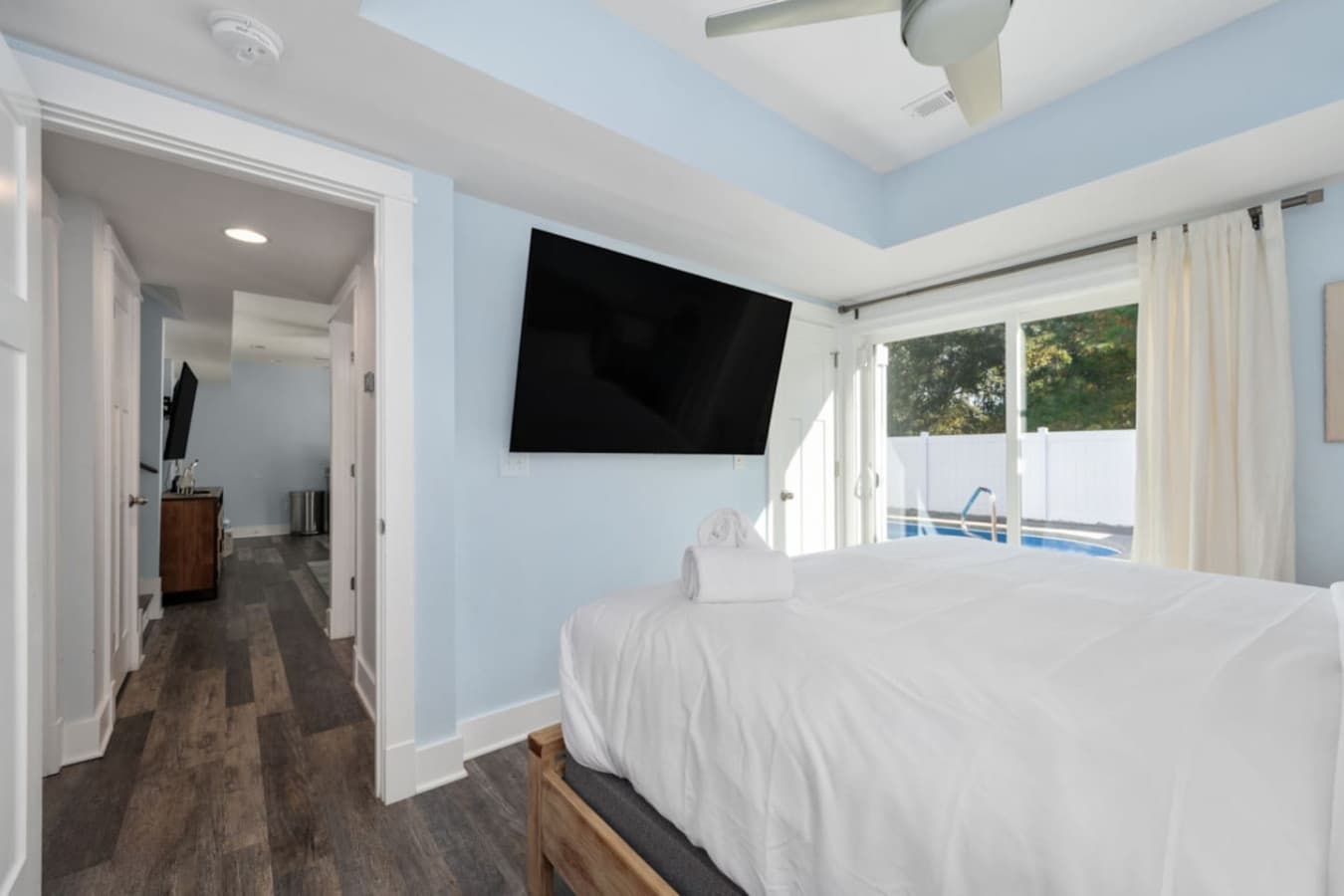 Bright bedroom w/ mounted TV, ceiling fan & natural light pouring in
