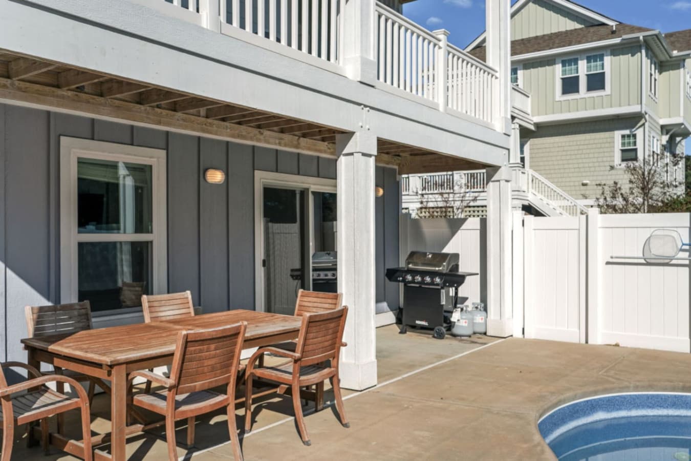 Covered ground-level patio w/ six-seat wood dining table, gas grill & the pool right alongside.
