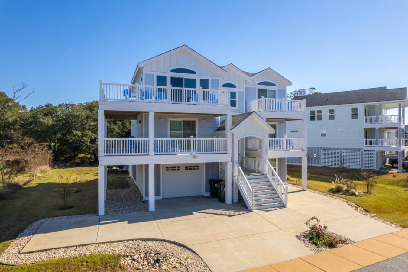 Elevated beach house w/ tiered decks, ground-level parking & a curved concrete driveway.