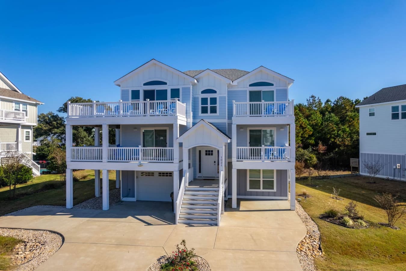Front elevation w/ two levels of covered porch, arched windows & a wide concrete driveway.