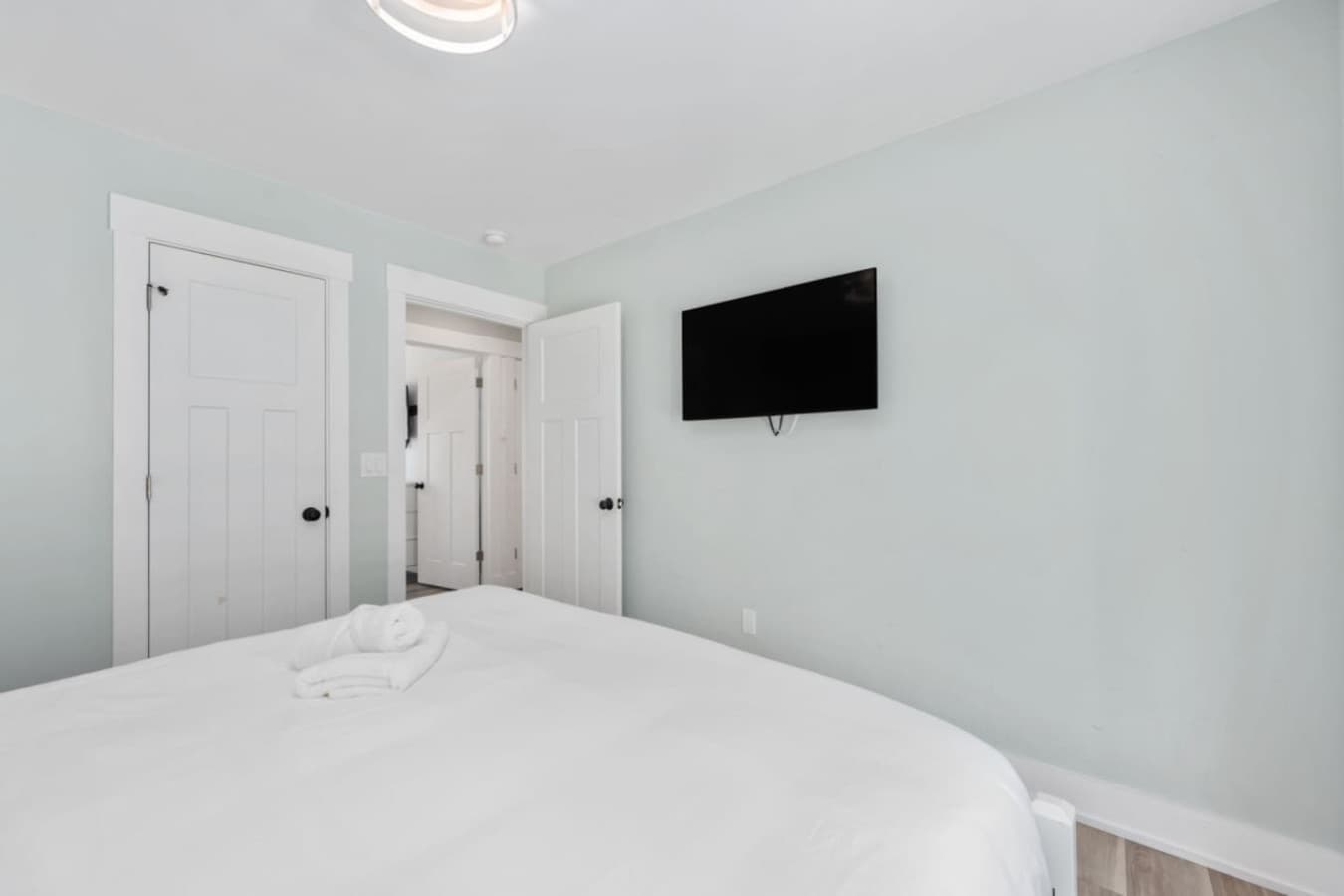 Comfortable bedroom setup w/ wall-mounted TV & easy closet access.