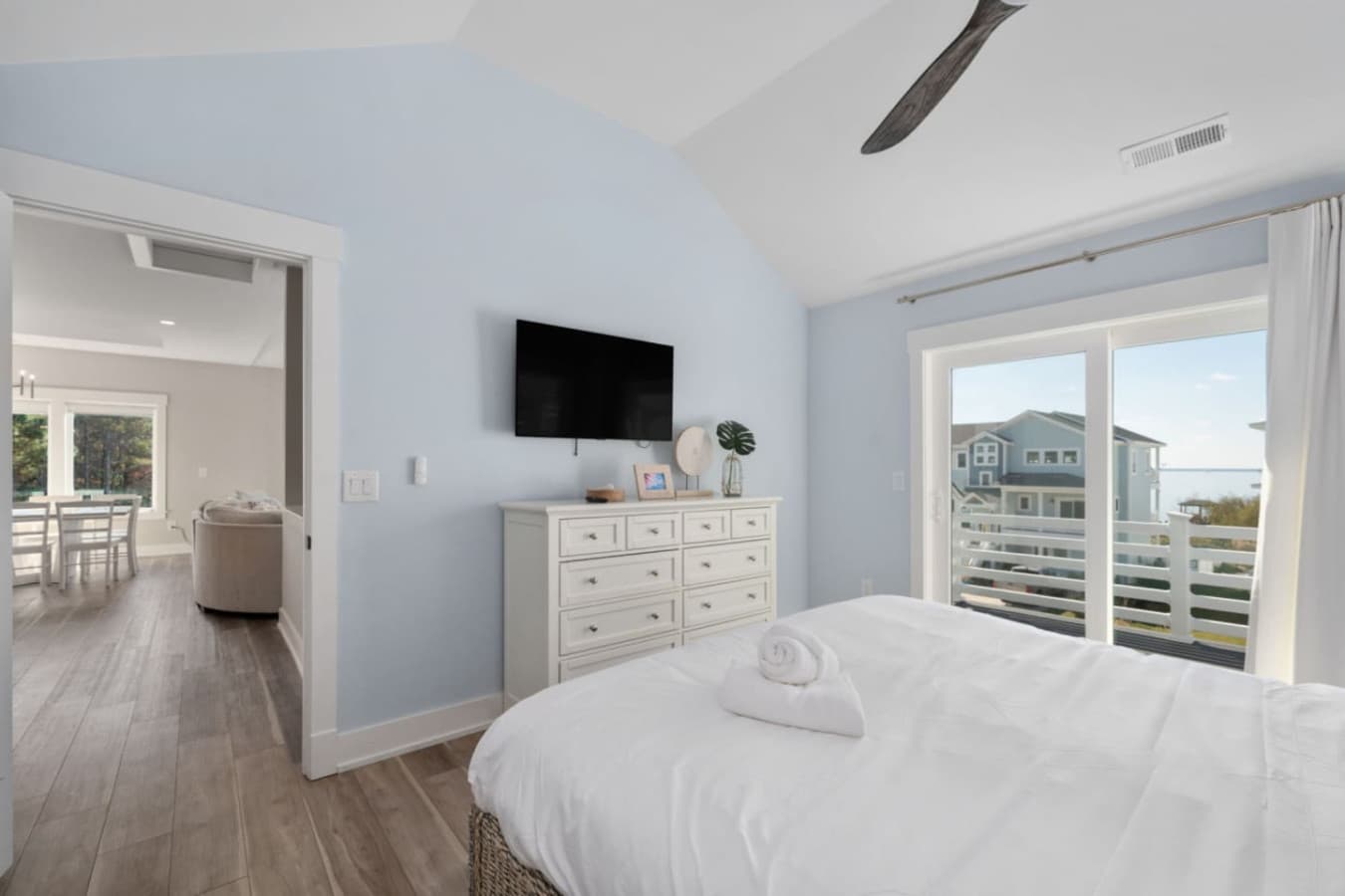 Bright bedroom w/ dresser, wall-mounted TV & doors opening to the balcony.