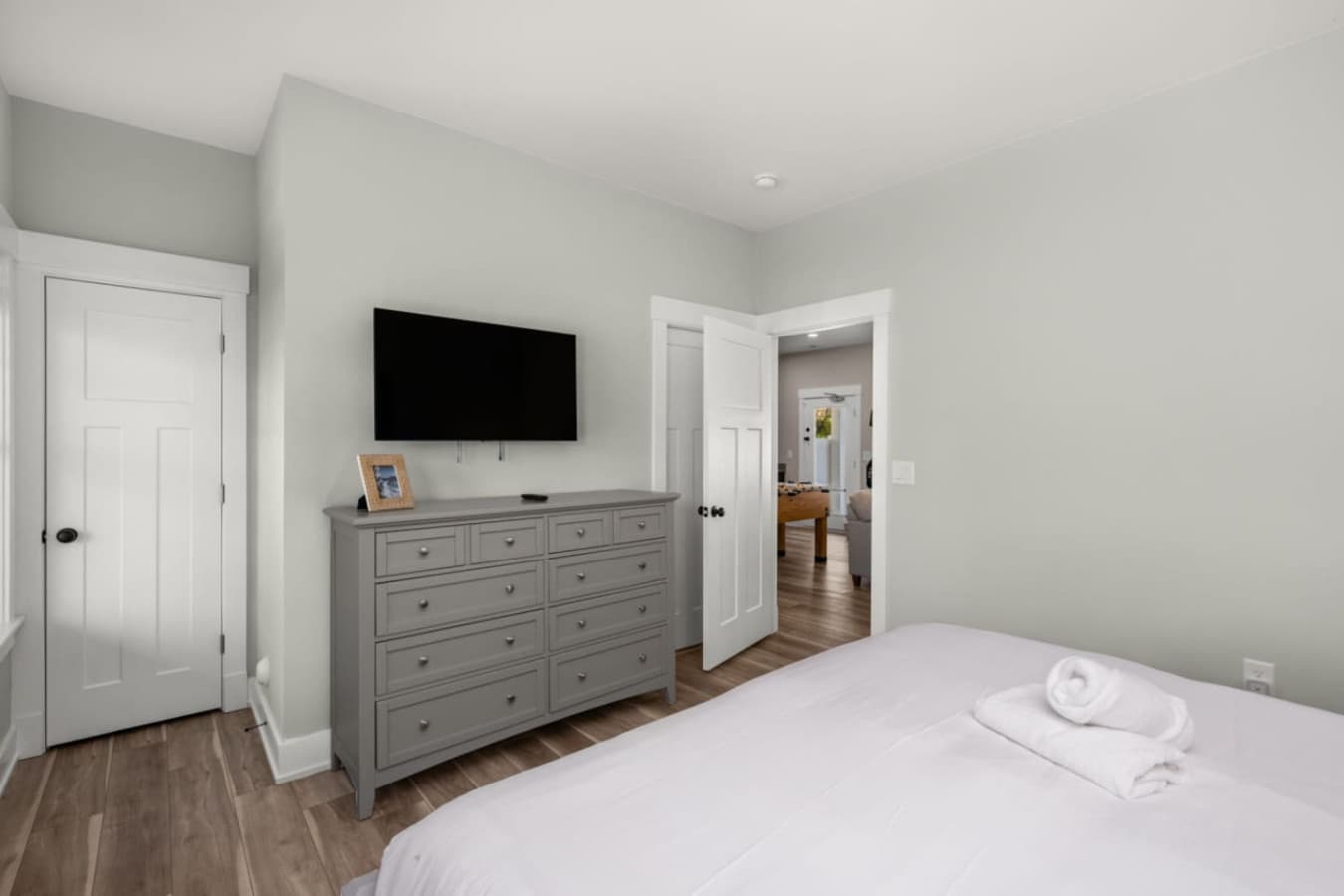 Comfortable bedroom w/ dresser, wall-mounted TV & calm neutral tones.