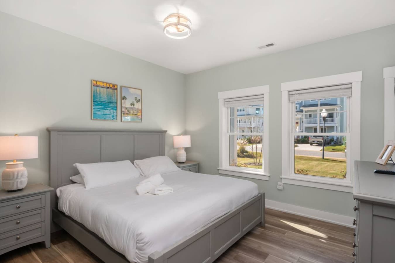 Calm, airy bedroom w/ a comfy bed, soft lighting, & sunny windows that brighten the space.