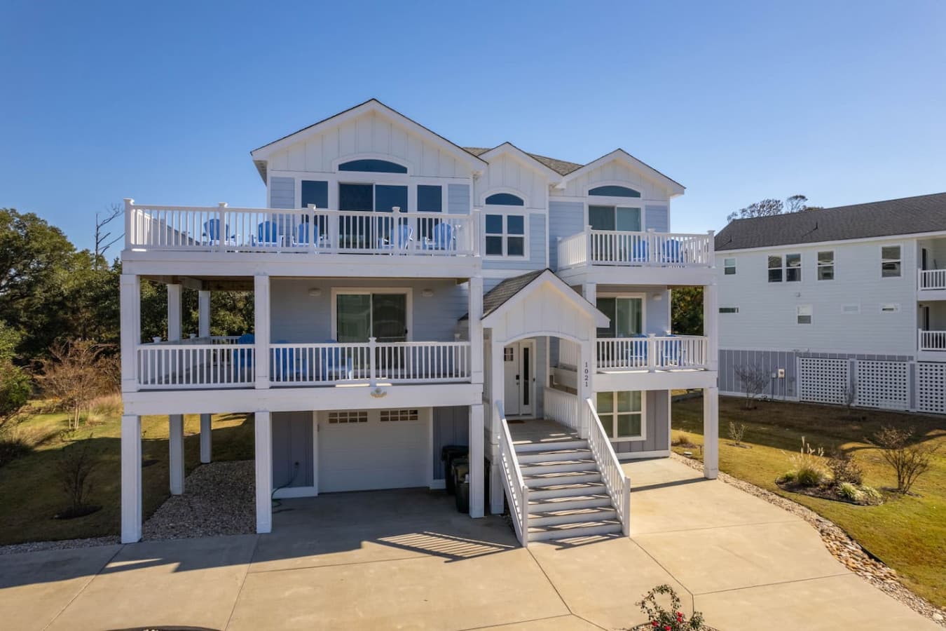 Front elevation w/ wide entry stairs, twin balconies & shaded parking underneath.