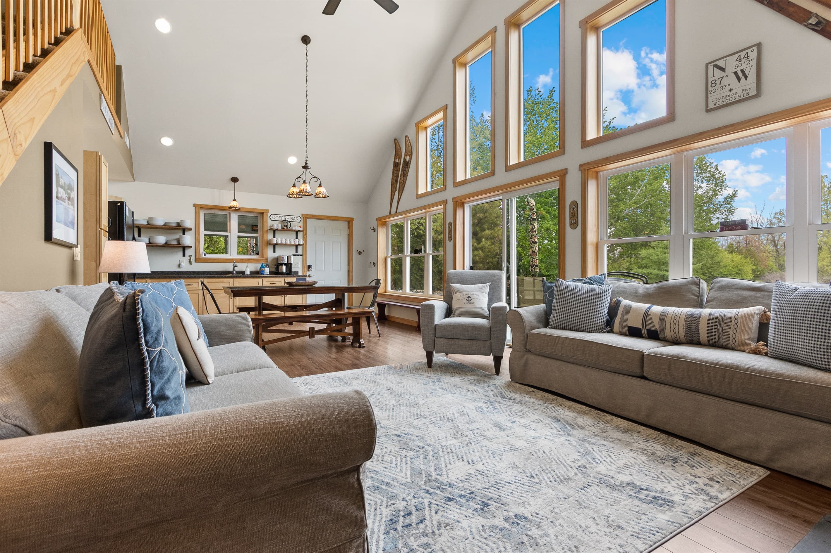 The whole main floor in a single look — living room, dining table, kitchen, Coffee Bar, and a wall of windows bringing Sawyer Harbor in from every angle. Ten guests, one space, zero compromise.