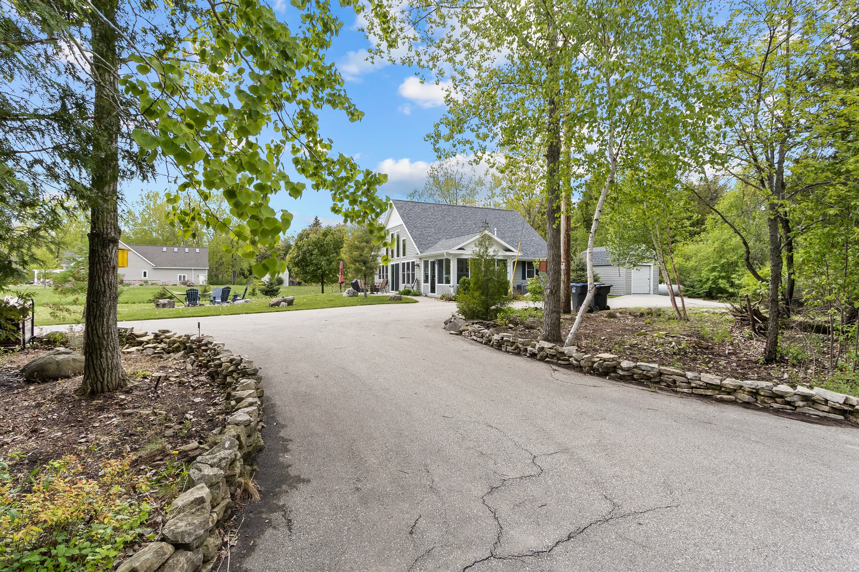 The driveway pulls you in and the cottage waits at the end — fire pit chairs already visible, Sawyer Harbor just past them. This is what a Door County arrival should feel like.