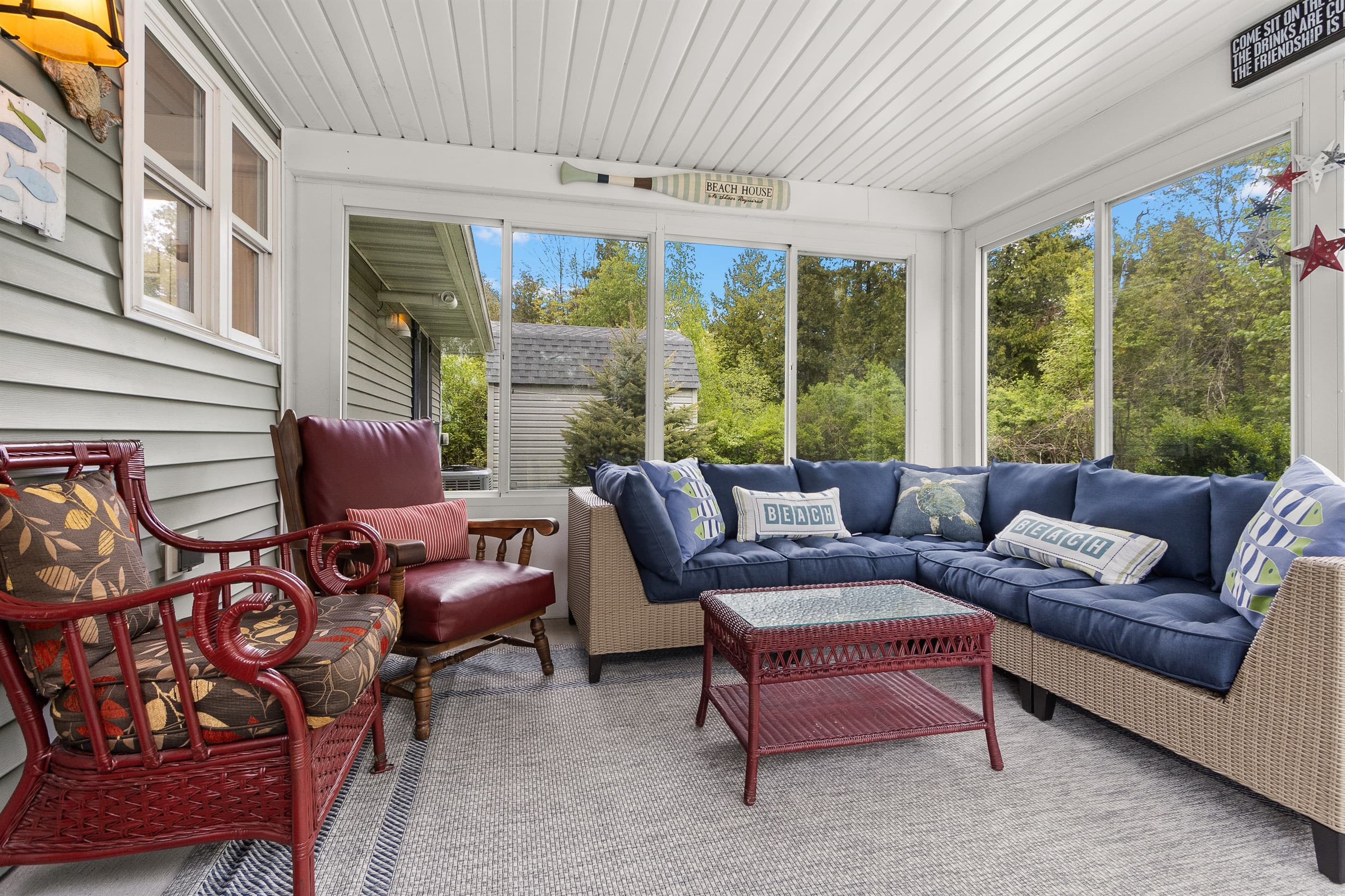 The sign above the door says 'come sit on the porch' — it's not wrong. The sectional fits the group, the windows bring in the trees, and there's no good reason to leave once you're settled.