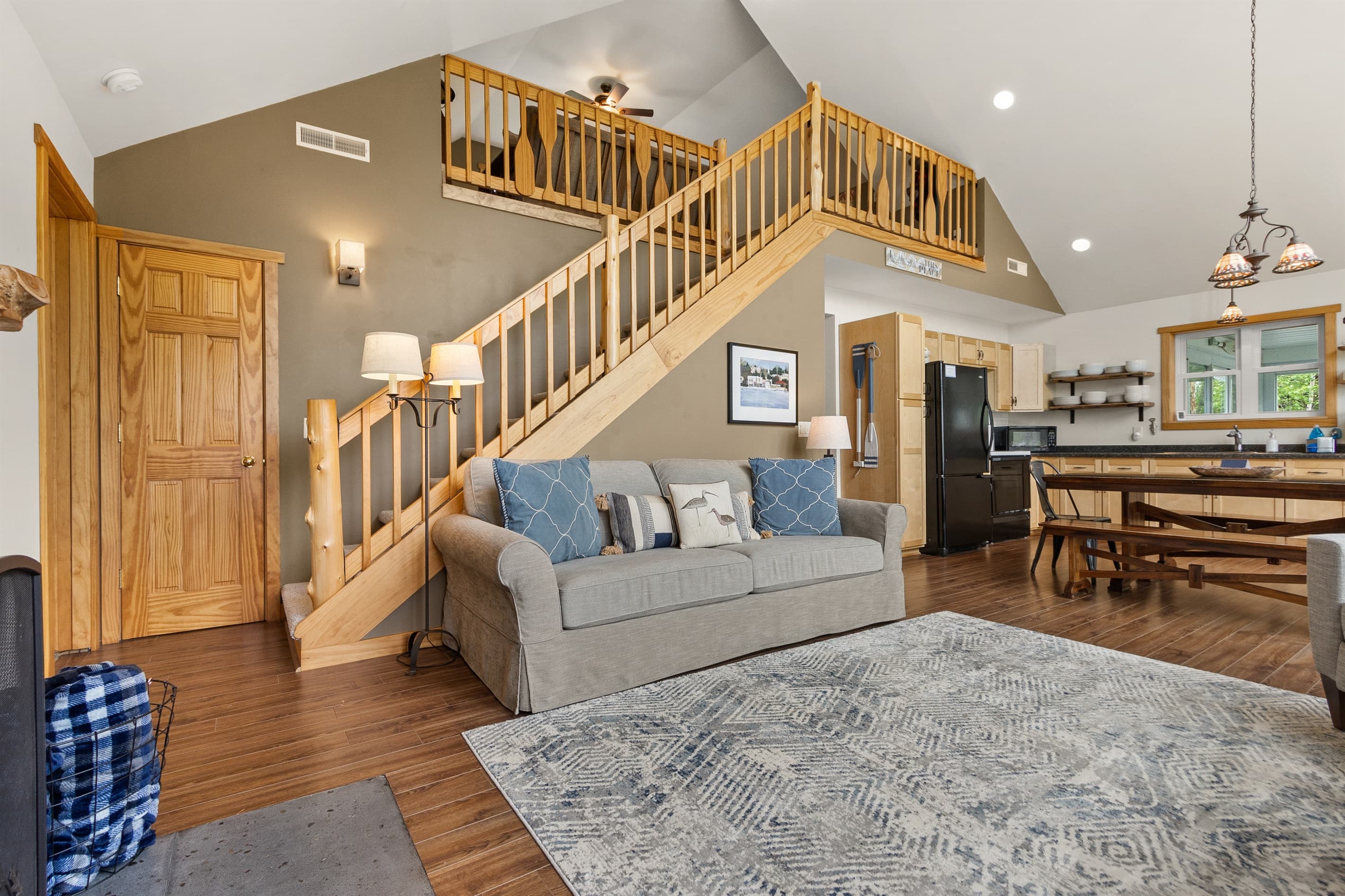 The great room connects everything — sofa, staircase to the loft, kitchen around the corner, and the harbor through the windows. One open floor plan, ten guests, and nowhere to feel crowded.