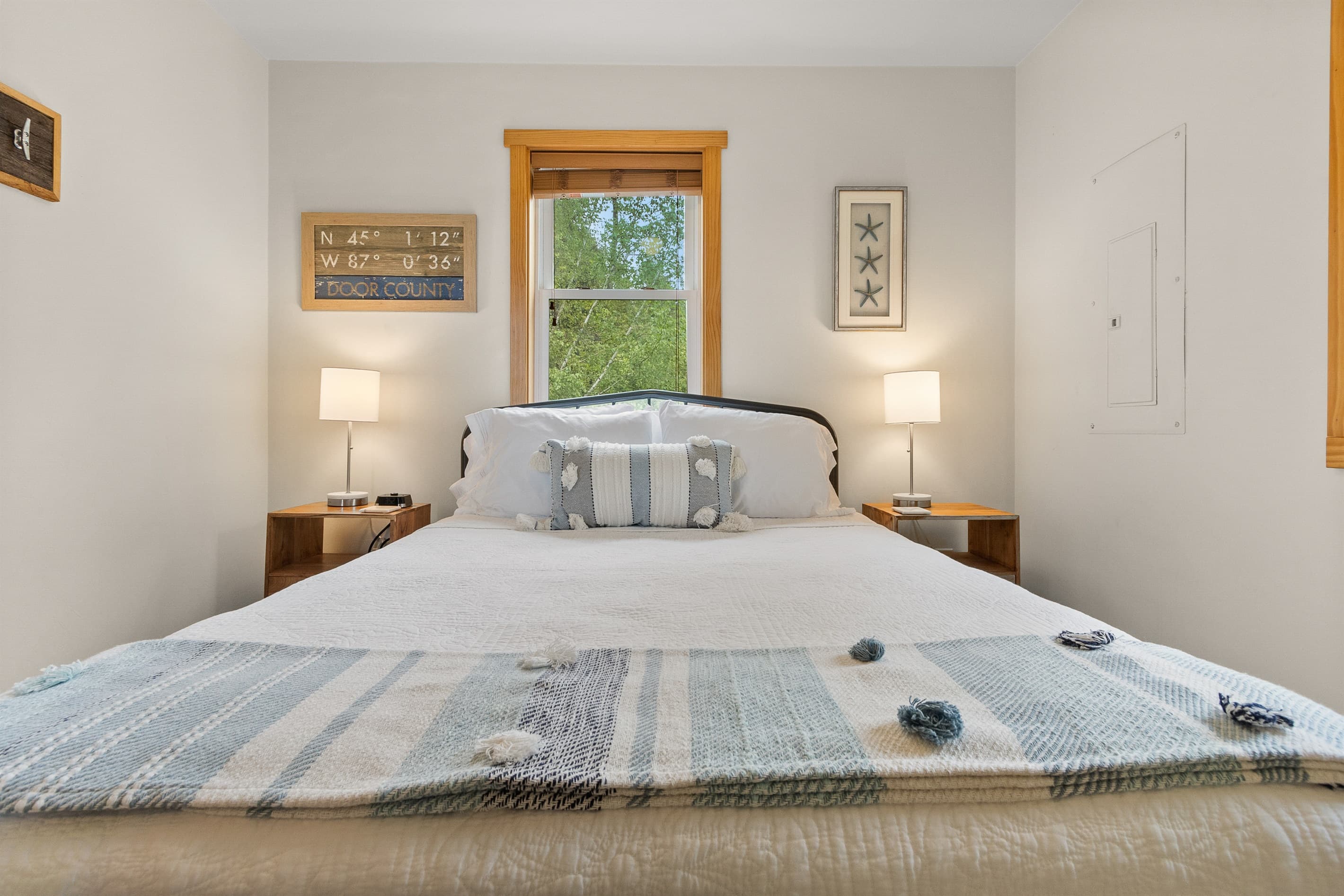 A quiet queen bedroom with Door County's exact coordinates on the wall. Main floor, private, and a short walk to the coffee bar. The sign above the bed says exactly where you are.