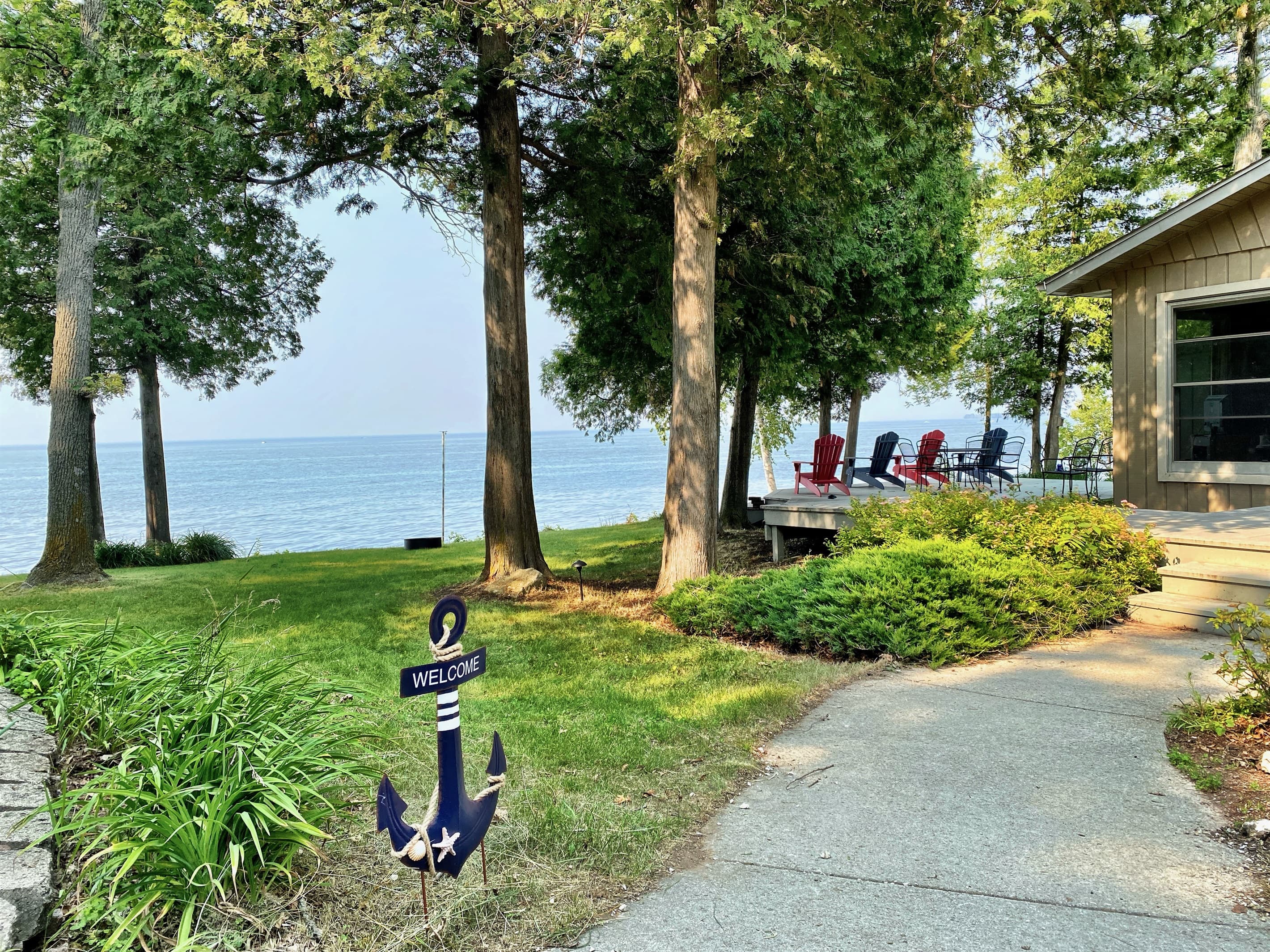 Waterfront deck dining at Rocky Shores Retreat — wrought iron table and chairs with bay views through mature trees. Outdoor entertaining space, Door County WI, sleeps 10.