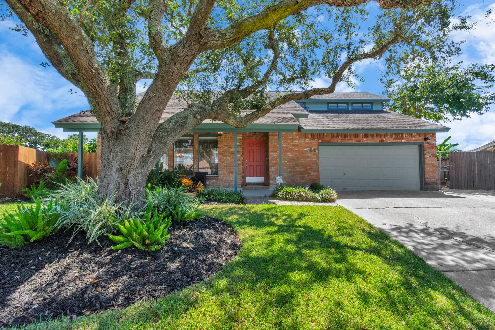 Classic Galveston charm at Lakeview Landing — lush manicured landscaping and a magnificent oak tree frame the entrance at 44 Lakeview Drive.