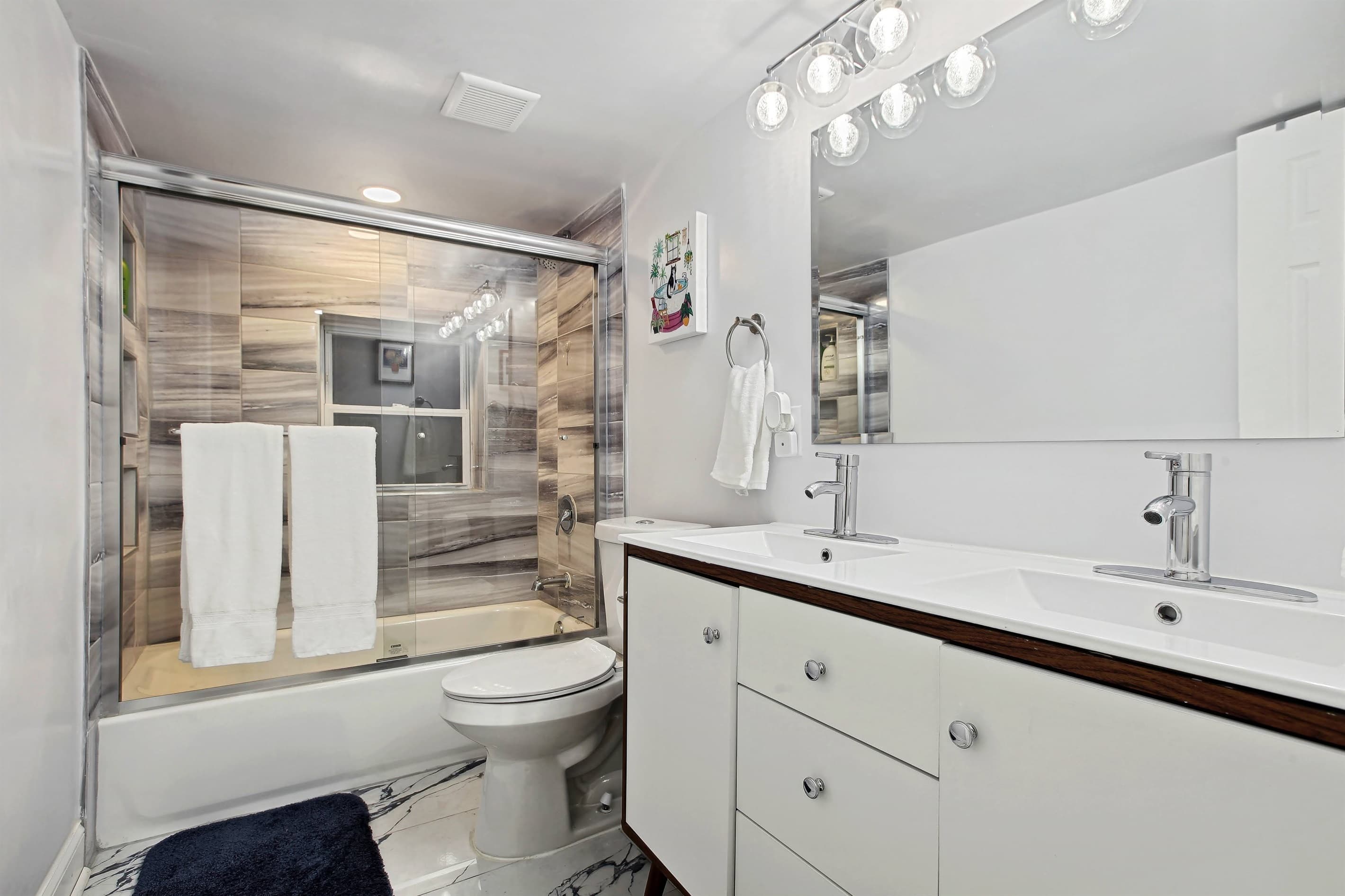 This full bathroom has a tub with glass doors and a double vanity