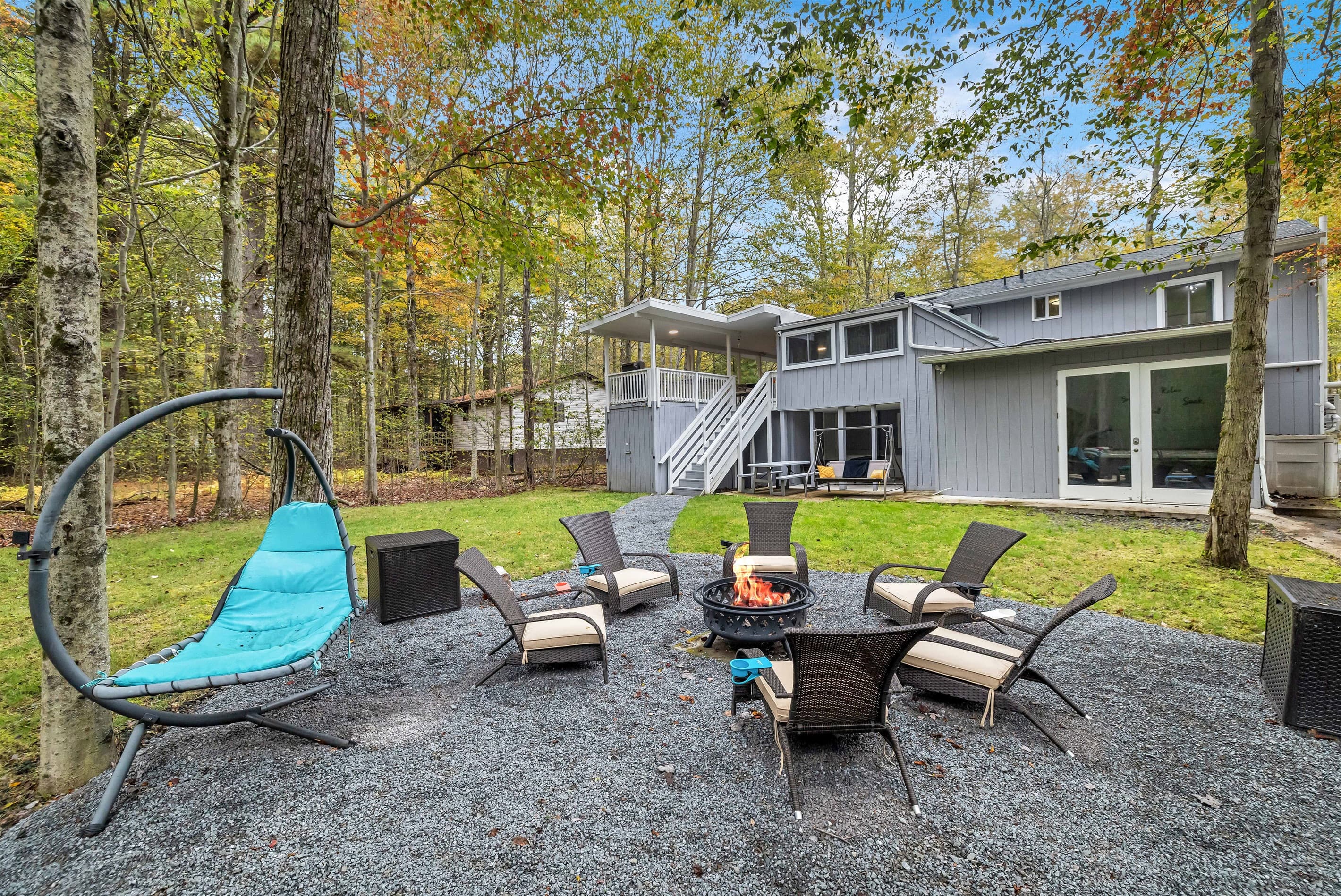 Relax in the spacious backyard featuring a firepit, chairs, and loungers, all with a serene forest view.