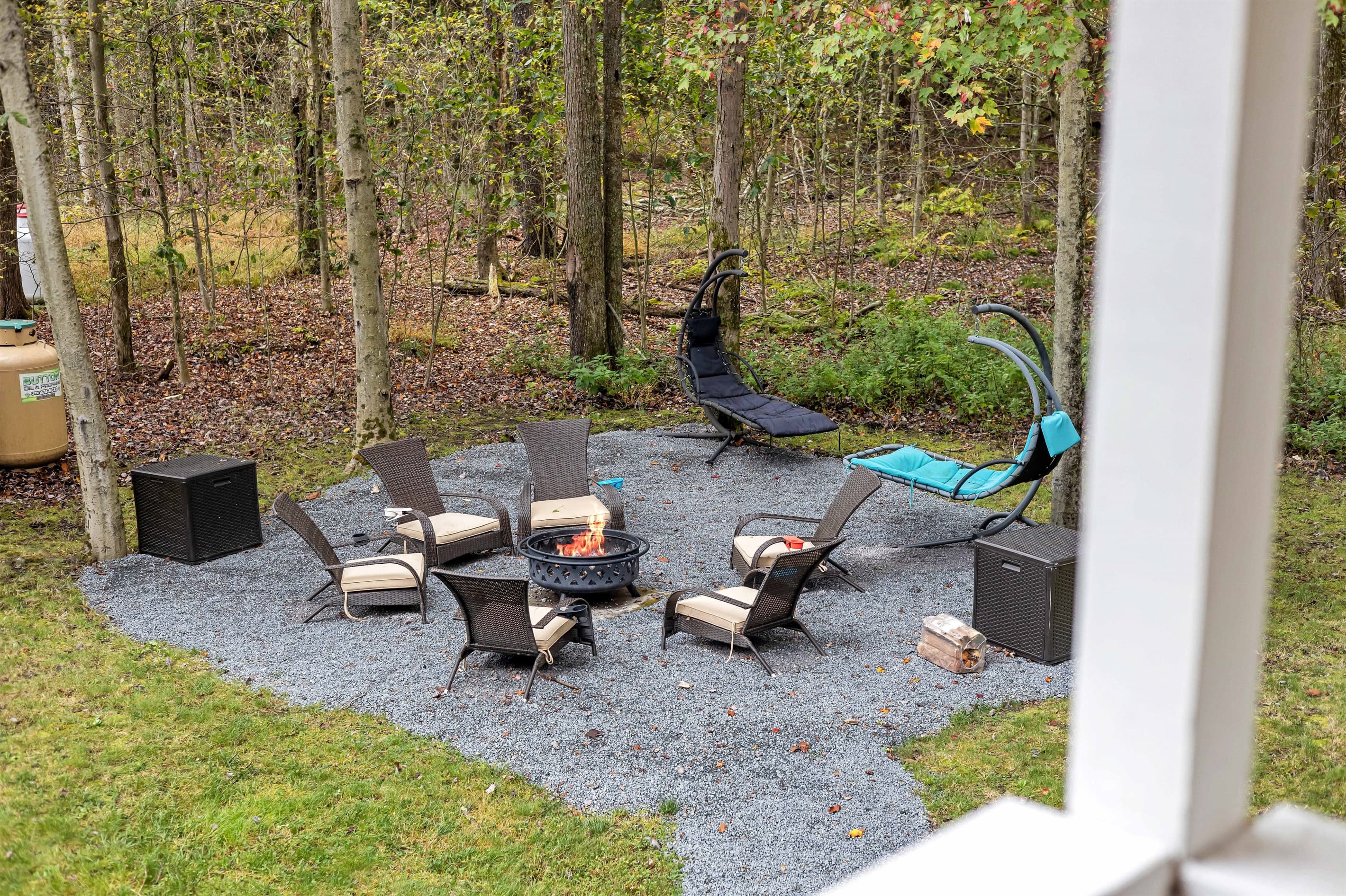 Relax in the spacious backyard featuring a firepit, chairs, and loungers, all with a serene forest view.