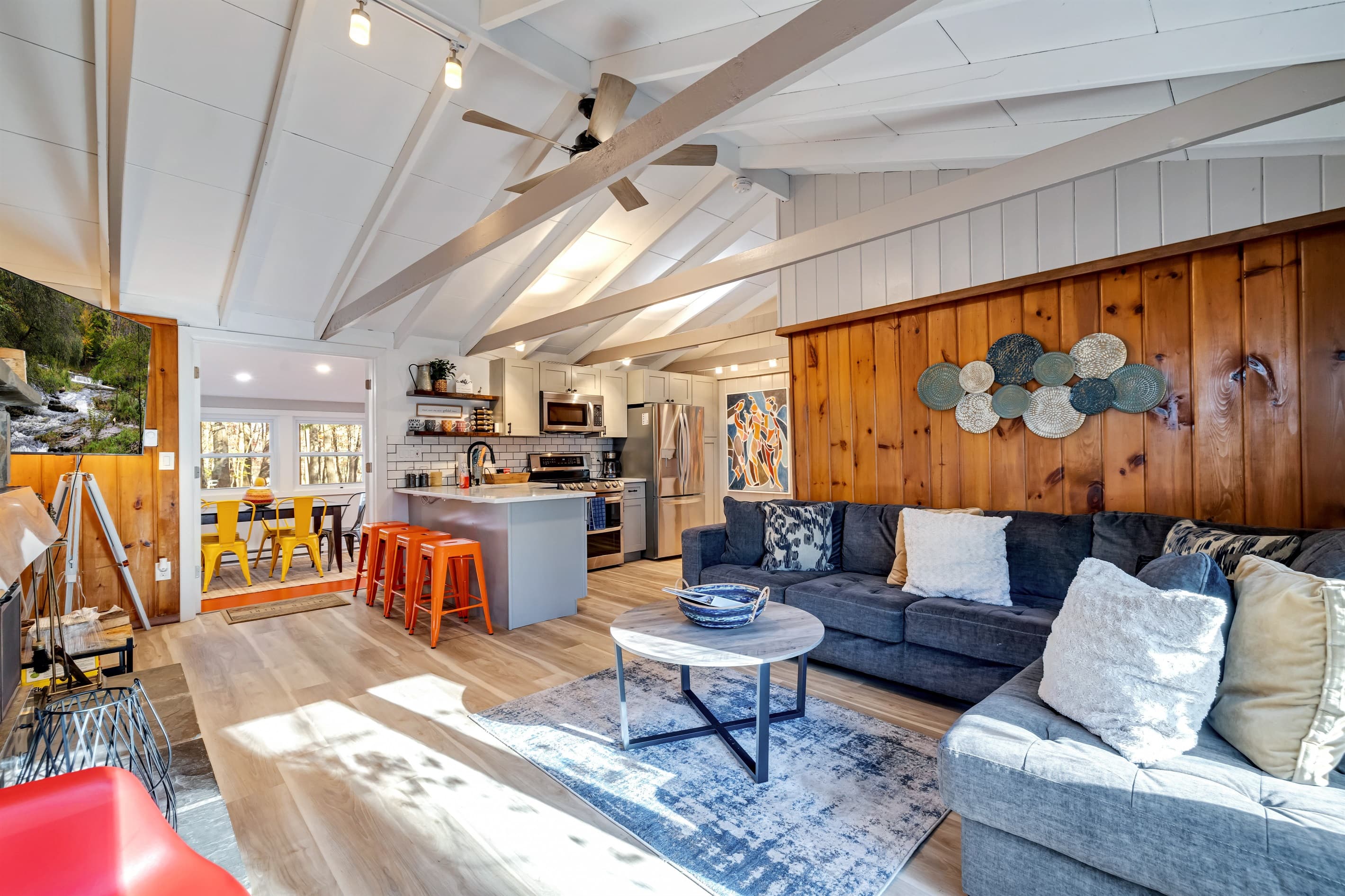 Cozy living room featuring a large screen TV, AC, and a wood-burning fireplace, complemented by a comfortable sectional sofa and rustic wood paneling for a warm, inviting atmosphere.