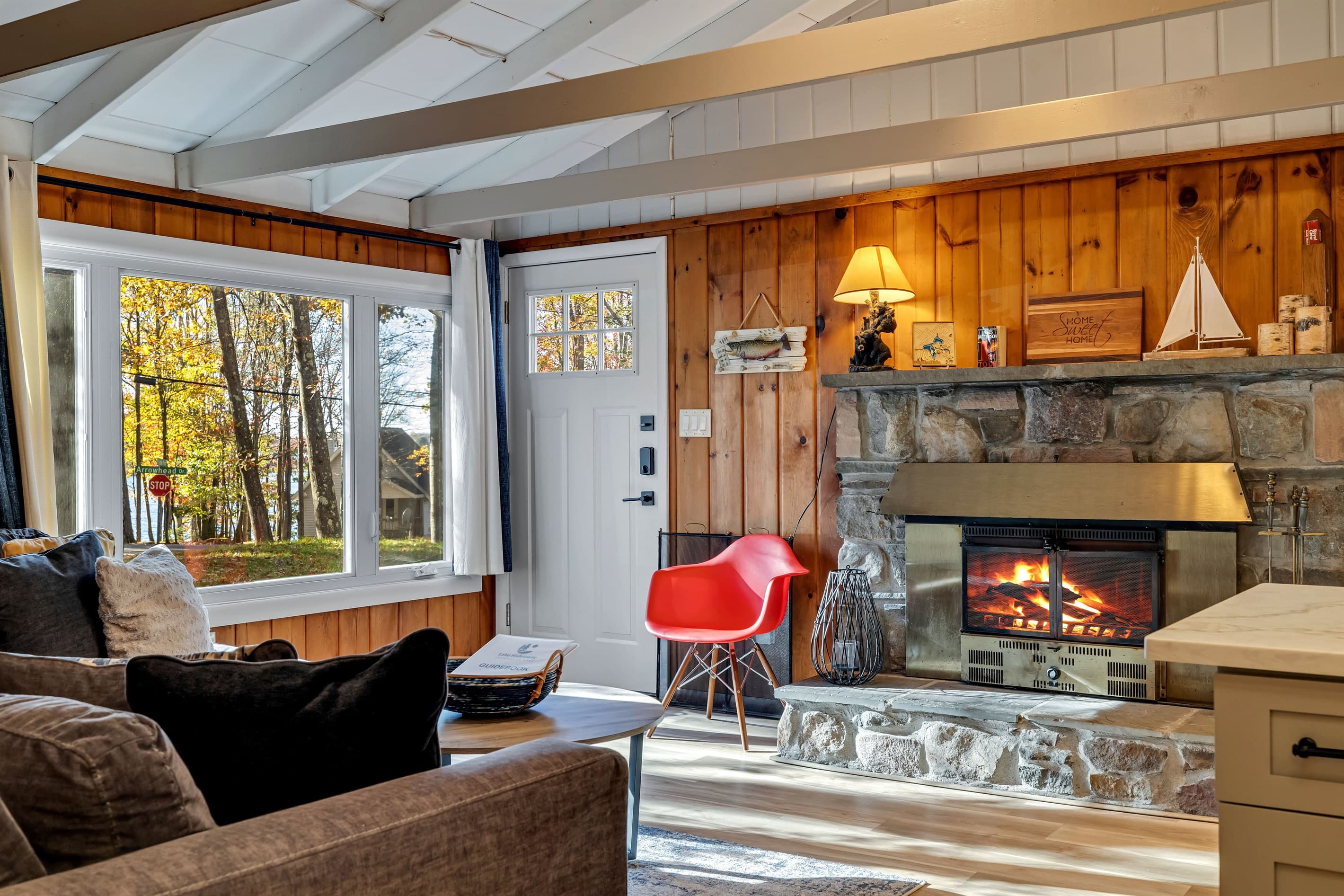 Cozy living room featuring a large-screen TV, AC, wood-burning fireplace, and a comfortable sectional sofa. Rustic charm with wood paneling creates the perfect atmosphere for relaxation