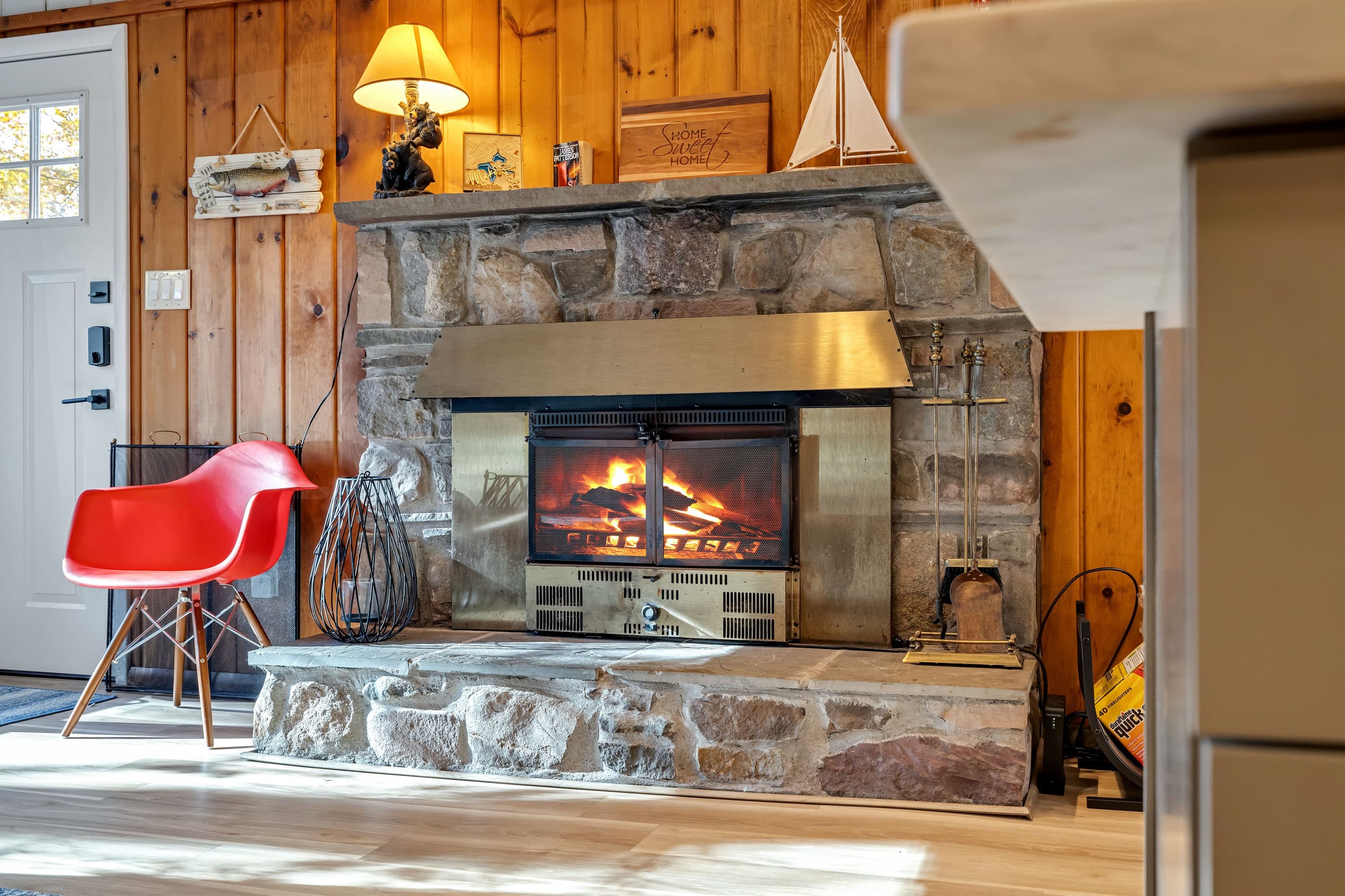 Cozy living room featuring a large-screen TV, AC, wood-burning fireplace, and a comfortable sectional sofa. Rustic charm with wood paneling creates the perfect atmosphere for relaxation