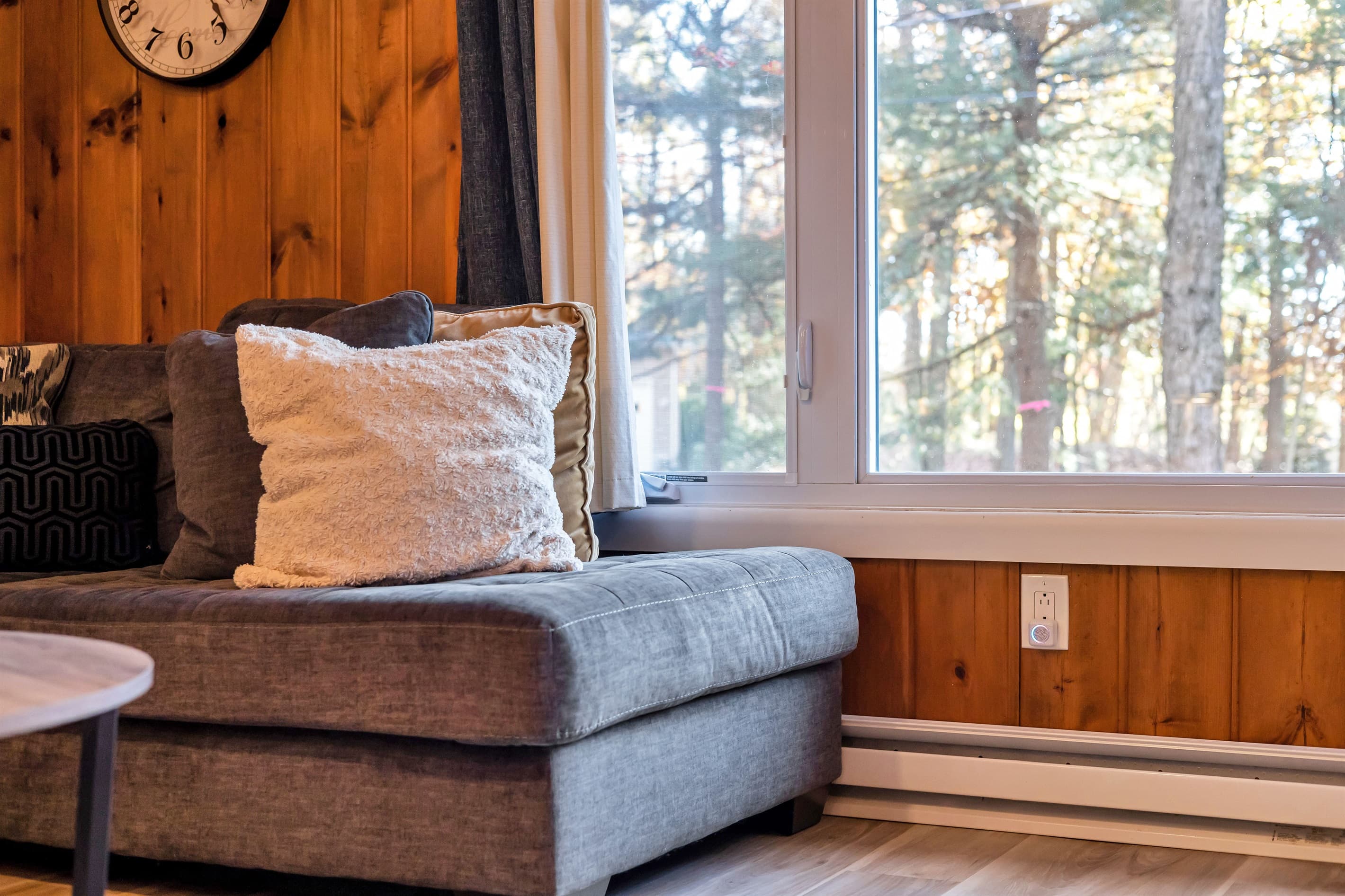 Cozy living room featuring a large-screen TV, AC, wood-burning fireplace, and a comfortable sectional sofa. Rustic charm with wood paneling creates the perfect atmosphere for relaxation.
