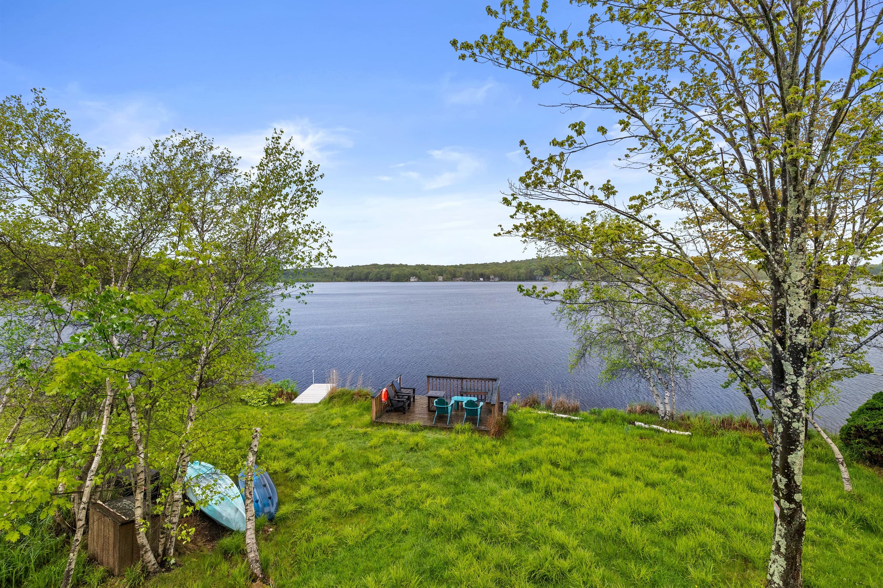 Lakefront backyard with a grassy lawn, spacious deck overlooking the water, and a private dock for relaxing or launching a kayak.