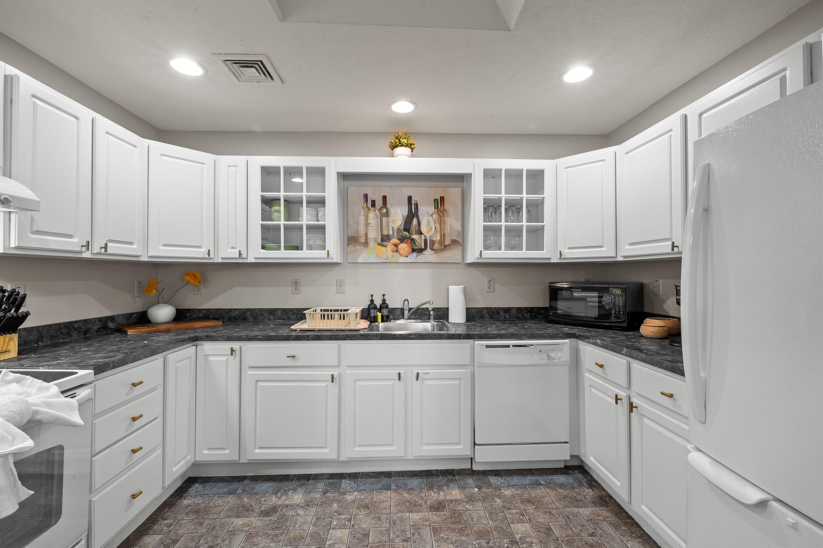 Fully stocked kitchen with white appliances, stainless sink, dishwasher, microwave, toaster, and coffee maker.