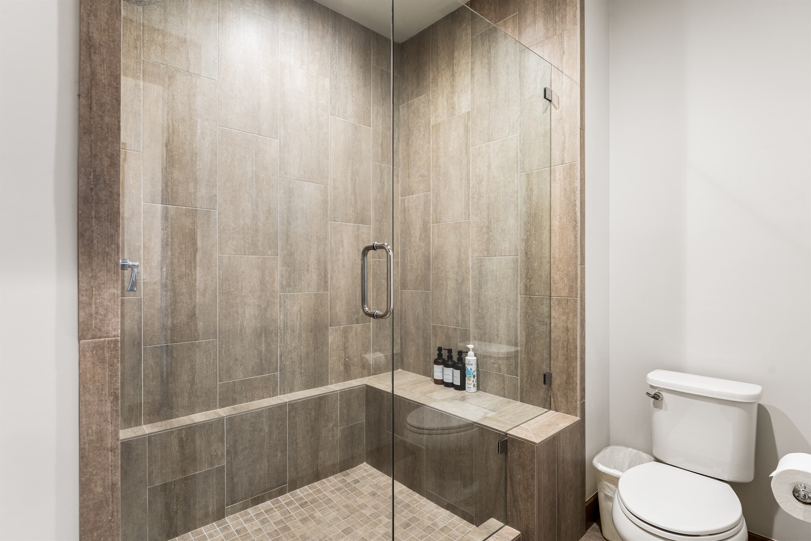 This bathroom features dual vanities and a spacious walk-in shower, providing both style and functionality. Thoughtfully stocked with shampoo, conditioner, and body wash for a comfortable stay.