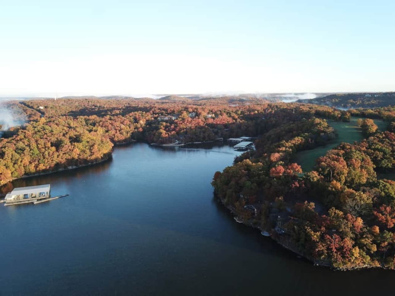 This expansive aerial view showcases the stunning Lake of the Ozarks, surrounded by vibrant fall foliage, offering a truly picturesque setting. The property boasts multiple boat docks, providing convenient access to the water for all your aquatic adv