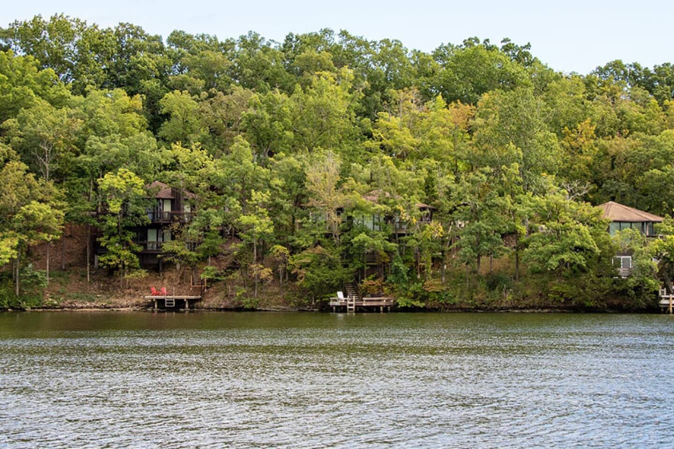 This aerial view captures a charming lake house nestled among lush trees, offering a tranquil escape. A red and white boat cruises on the water, suggesting the lake's recreational opportunities for potential renters.