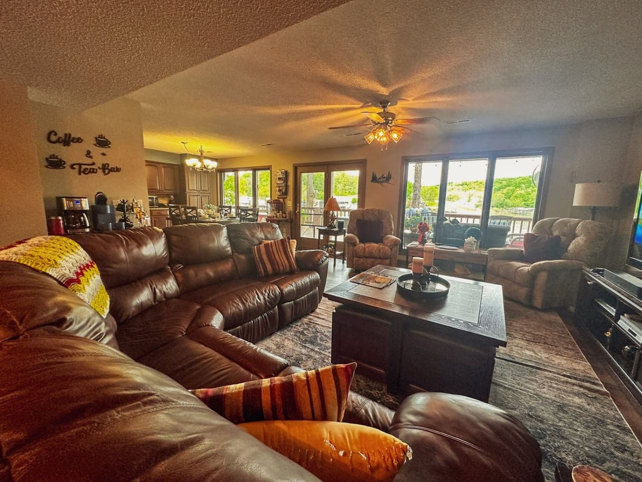 From this view, the living room feels even more inviting, with sunlight pouring in through big windows and highlighting the rustic charm. Cozy furniture, soft blankets, and natural wood accents make it the perfect spot to relax and feel right at home