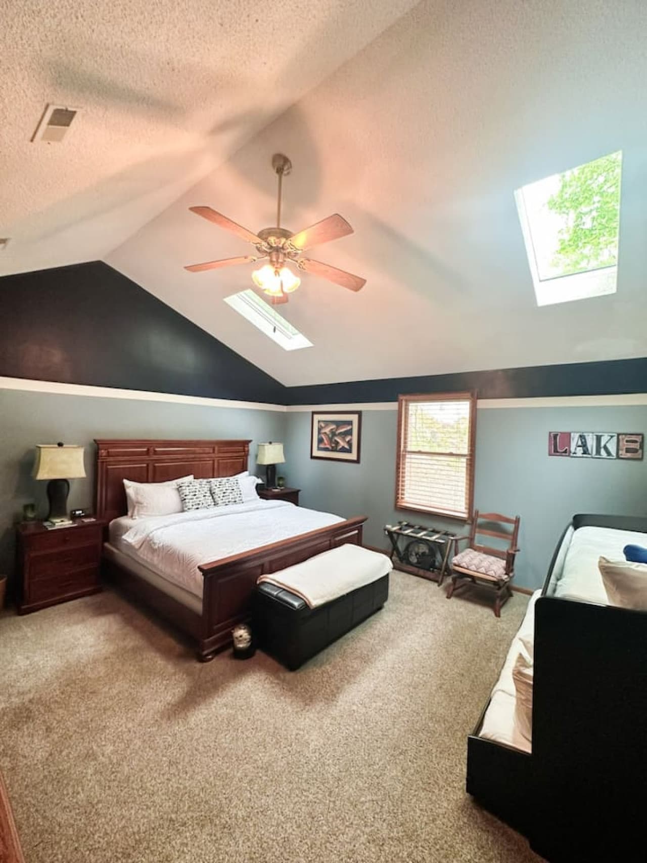 Unwind in this spacious and serene bedroom, featuring a plush king bed, cozy daybed, and soothing natural light from skylights above. With warm wood accents and soft carpet underfoot, it’s the perfect retreat after a day of lakeside fun. Comfort and
