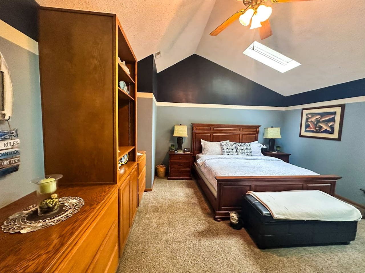 This rustic bedroom offers a full view of its spacious layout, featuring a large, inviting bed and a cozy bunk bed, all accented with a calming lake theme. Natural wood finishes, soft blues, and water-inspired decor create a tranquil, nature-filled a