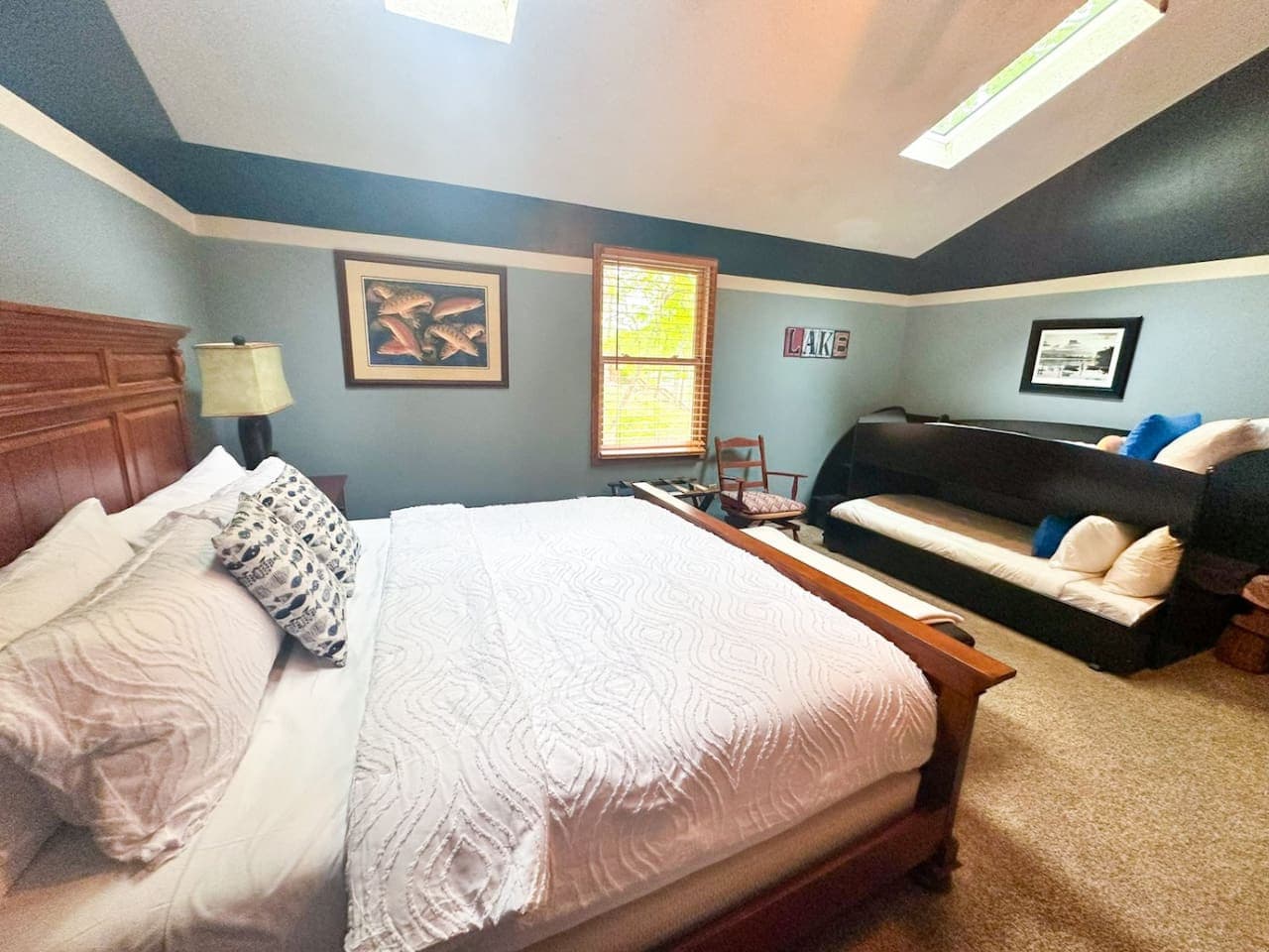 This rustic bedroom combines a huge, inviting bed with a charming bunk bed, all accented with a soothing lake theme. The natural wood elements and calming water-inspired colors create a peaceful, nature-filled retreat perfect for both relaxation and