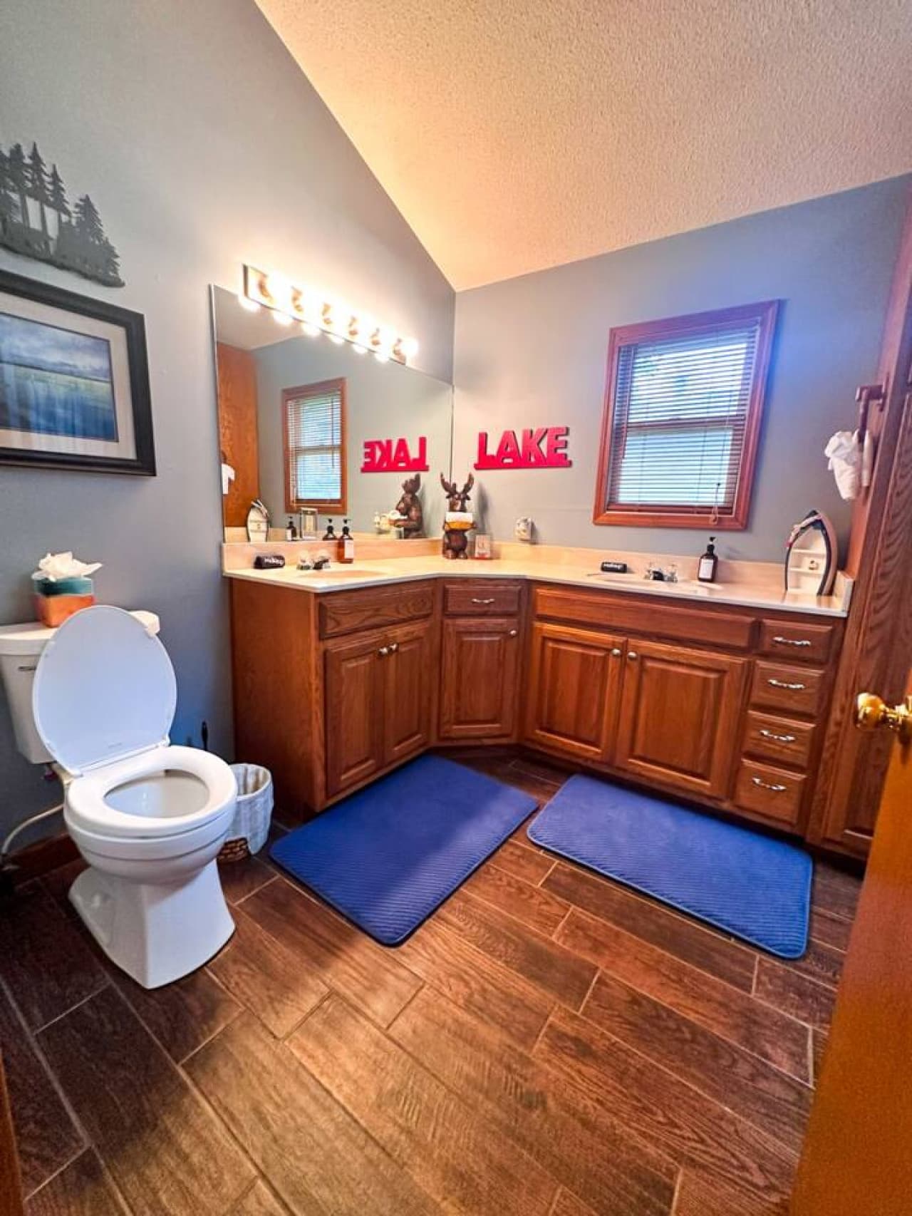 Relax in this cozy, lake-themed bathroom featuring double sinks, warm wood cabinetry, and inviting decor. A clean, comfortable space perfect for unwinding after a day by the water.