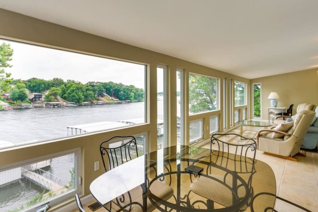 Enclosed sunroom with wall-to-wall windows offering breathtaking views of the serene lake, ideal for morning coffee or evening relaxation.