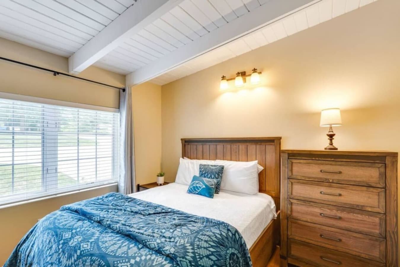 A bright and airy bedroom adorned with a teal quilt, rustic furnishings, and plenty of natural light.