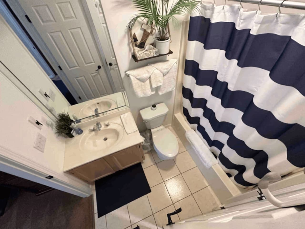 Bright and clean bathroom with a shower/tub combo featuring a stylish navy and white striped curtain, a spacious vanity, and handy shelving for your toiletries.