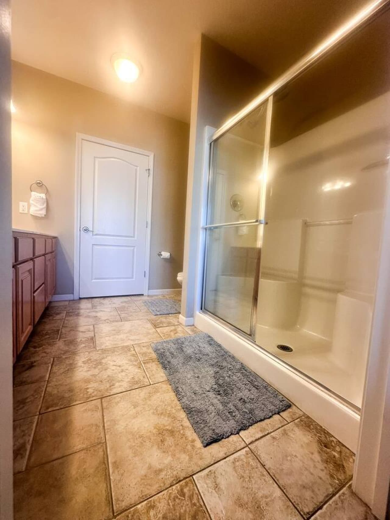 This spacious bathroom features a large, enclosed shower with a sliding glass door, providing a clean and inviting space. The tiled flooring and warm-toned walls create a welcoming atmosphere, complemented by a vanity with ample counter space.