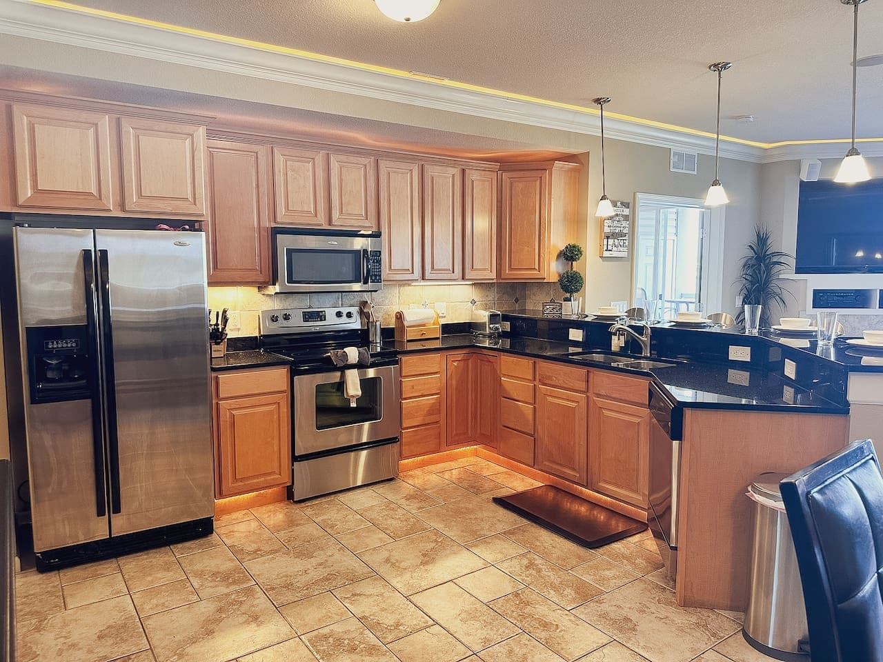 This modern kitchen is fully equipped with stainless steel appliances, including a spacious refrigerator, microwave, and oven, ready for all your culinary needs. The warm wood cabinetry and granite countertops create a functional and inviting space,