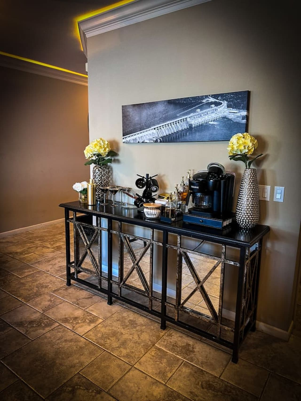This inviting coffee bar offers a fully equipped station for your morning brew, featuring a Keurig coffee maker and an array of accessories. Complementing the setup, two elegant flower arrangements add a touch of freshness and charm to the space.