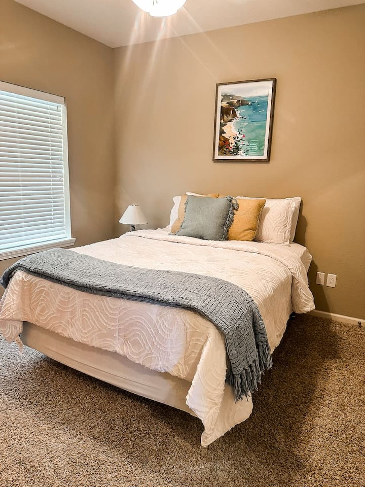 This bright and airy bedroom features a comfortable bed, adorned with inviting linens and soft pillows for a relaxing stay. The tasteful wall art and ample natural light from the window create a serene atmosphere, perfect for unwinding.