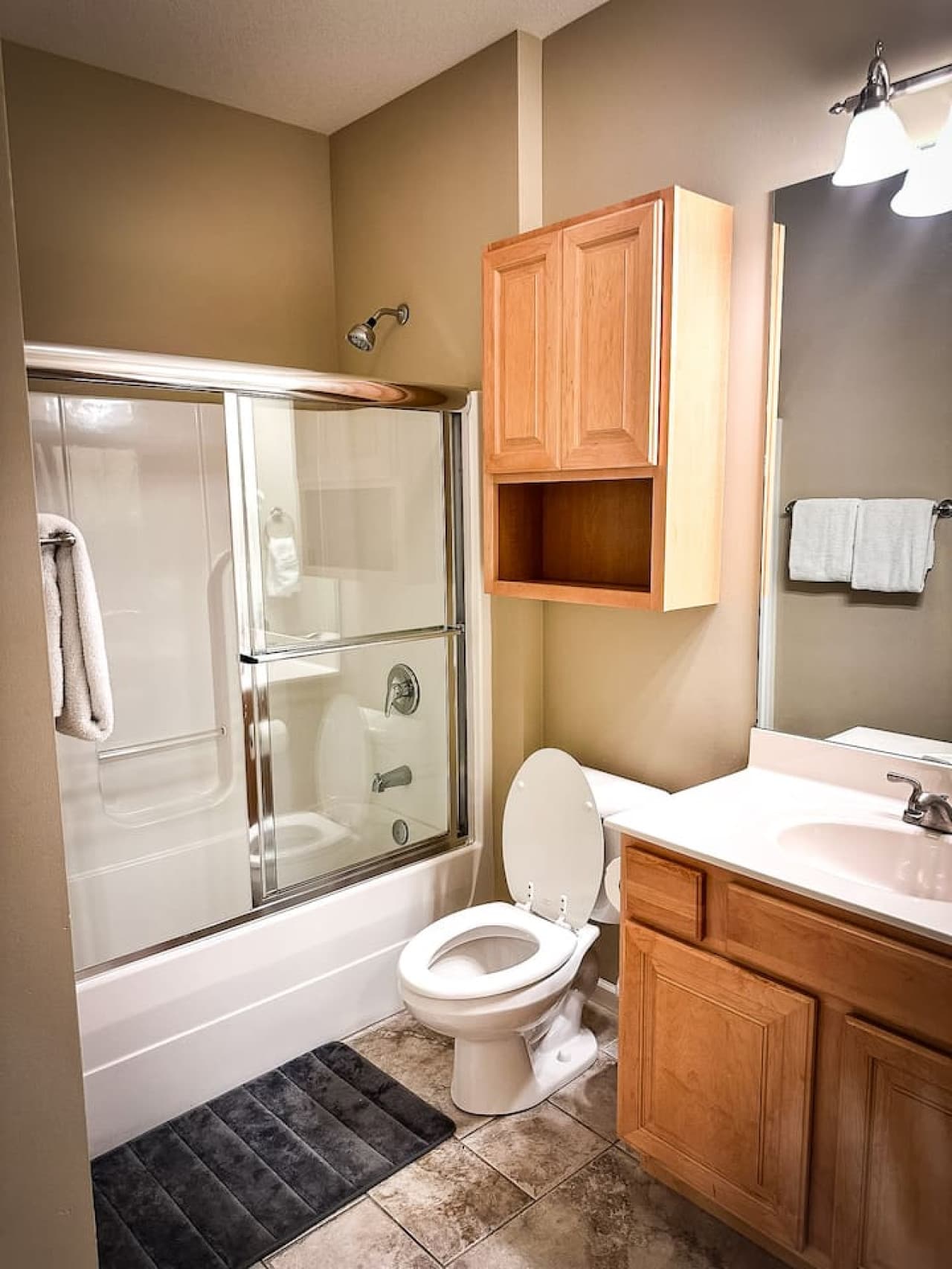 This clean and well-maintained bathroom features a convenient shower-tub combination with a sliding glass door for ease of use. Wooden cabinetry provides ample storage and a vanity with a sink offers plenty of counter space.