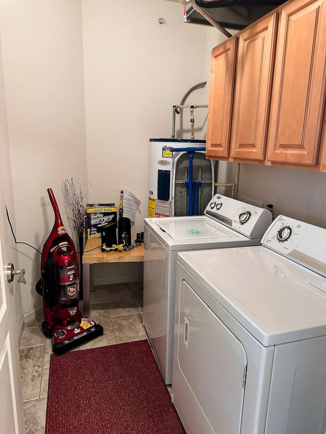 This functional laundry area is equipped with a convenient top-load washer and dryer, ensuring all your laundry needs are met during your stay. Adjacent wooden cabinets provide ample storage space for your essentials, keeping the area tidy and organi