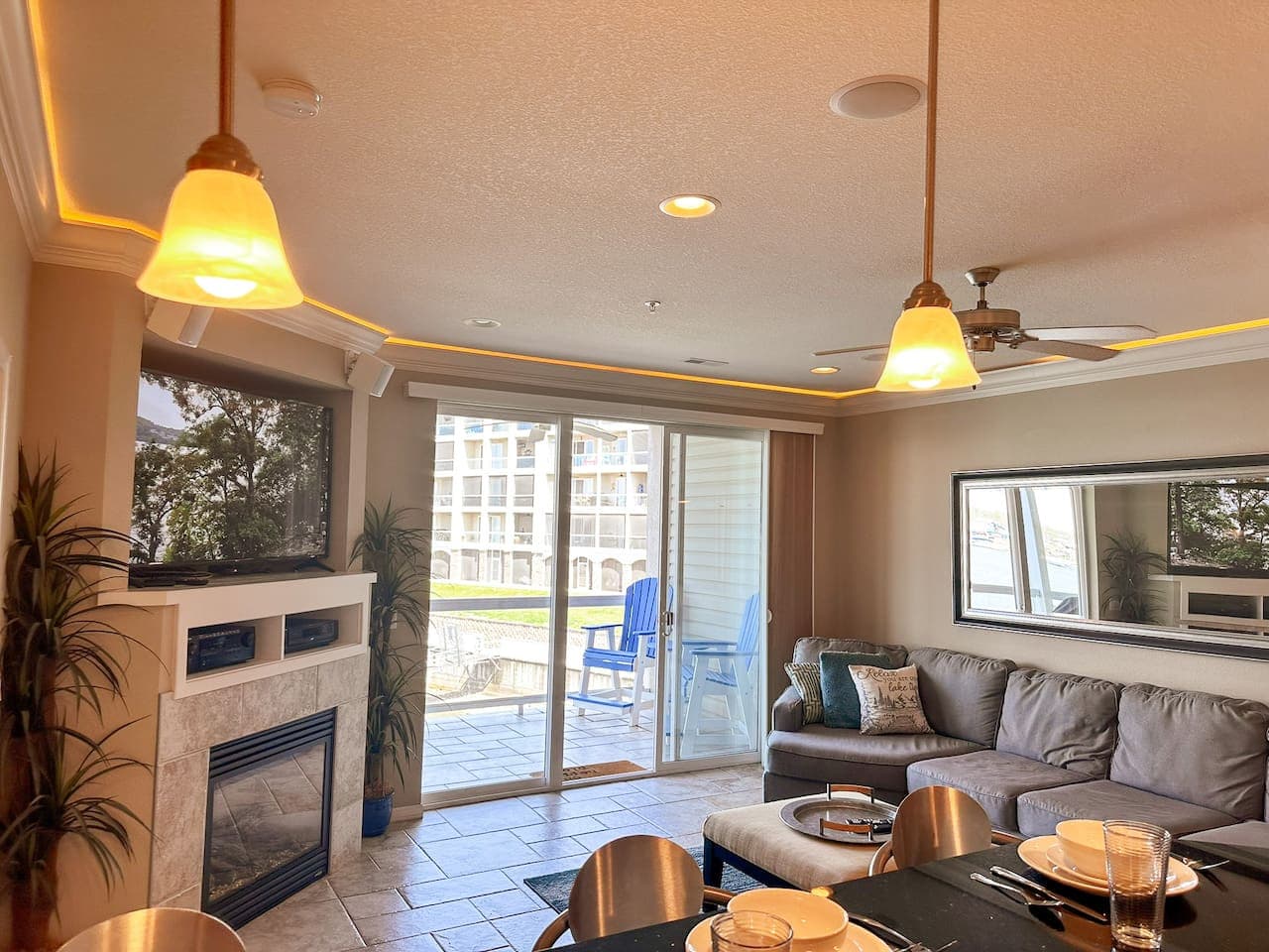 This welcoming living space features a cozy sectional sofa and a large flat-screen TV mounted above a modern fireplace, ideal for relaxing evenings. The sliding glass doors open onto a private balcony, offering serene views and ample natural light.