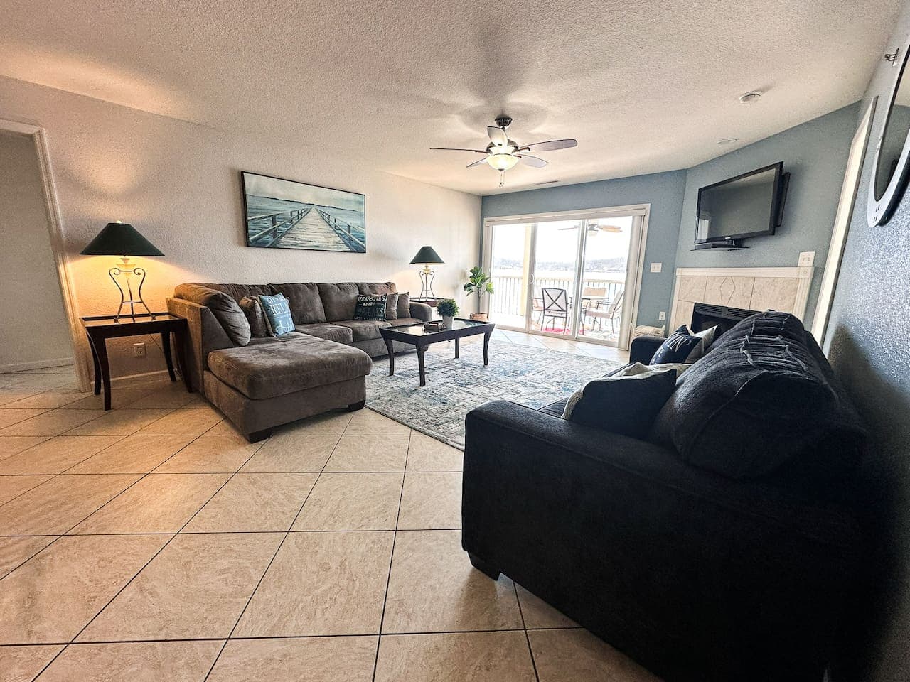 Large windows and a sliding door connect the cozy living room to the lakefront deck, offering expansive views and fresh air throughout the space.
