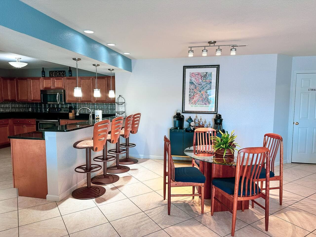 A spacious, open-concept kitchen and dining area featuring a sleek glass-top dining table, stylish pendant lighting, and a fully stocked coffee and beverage station.